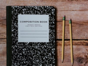 Composition book on desk with two pencils.